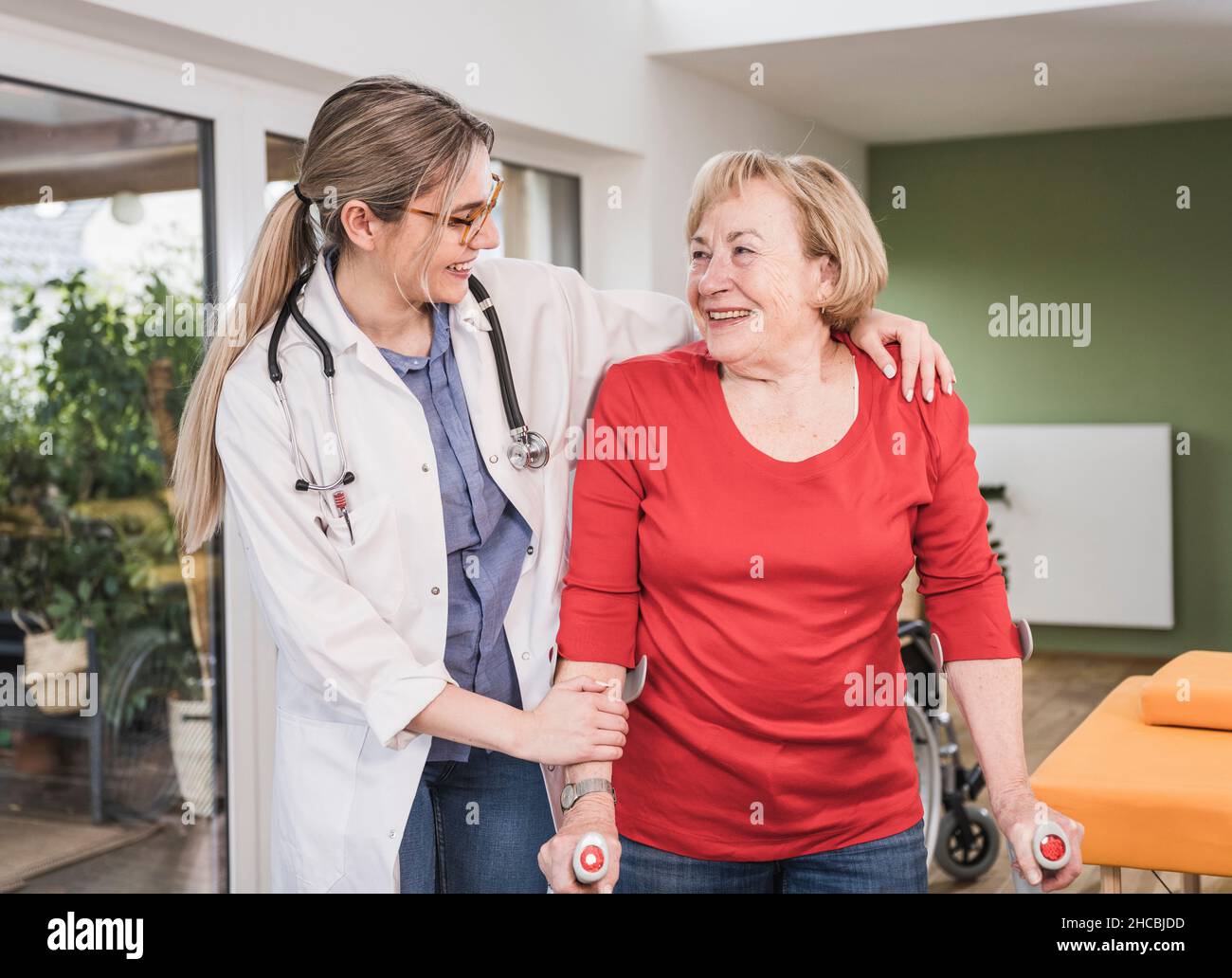 Doctor helping disabled woman standing with crutch at home Stock Photo