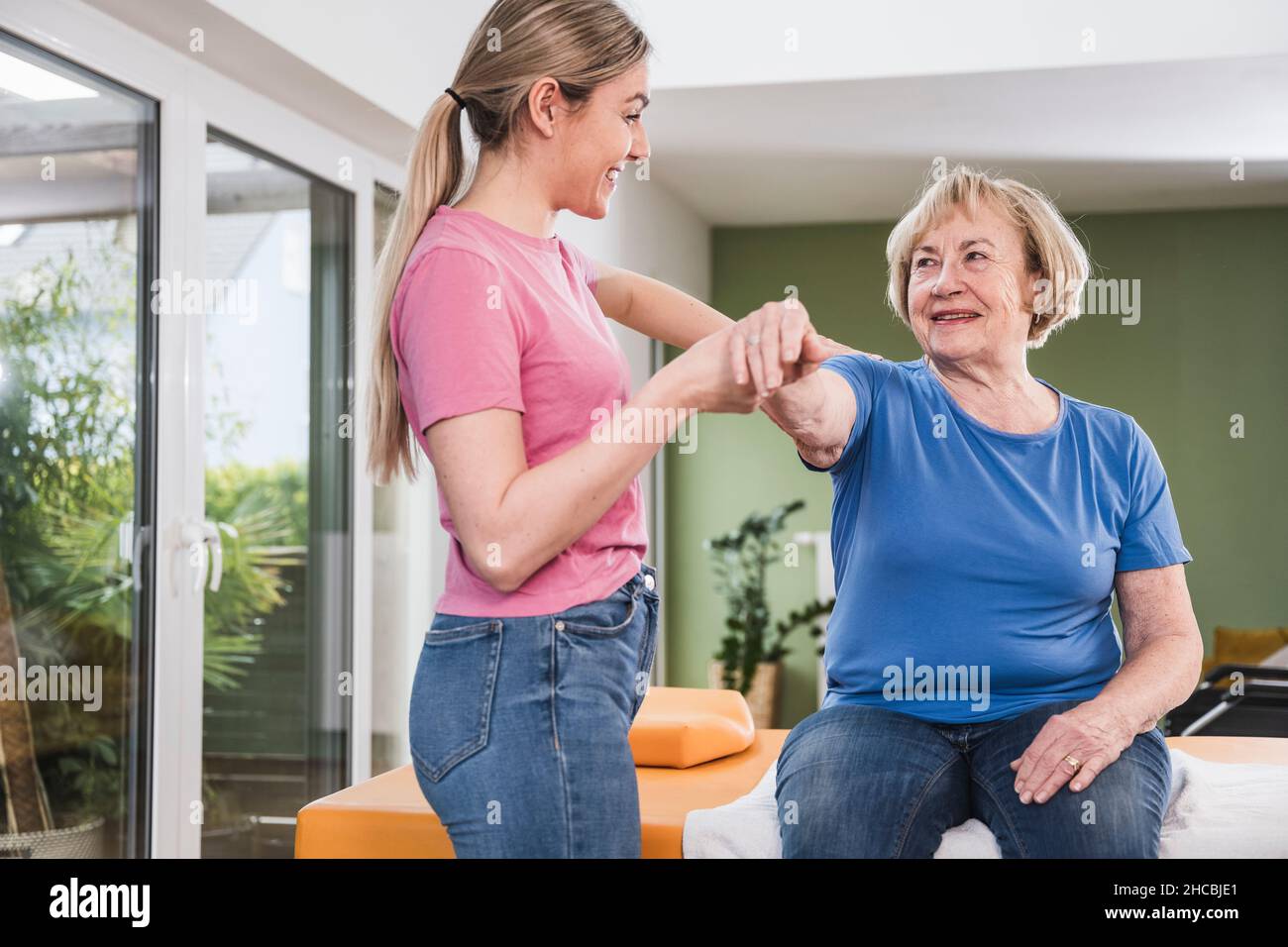 Smiling physical therapist supporting woman to exercise at home Stock Photo