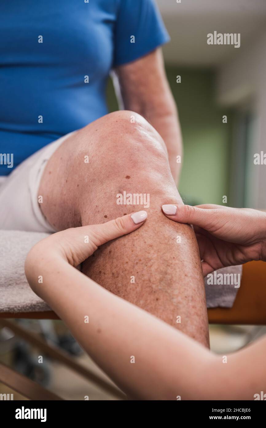 Physical therapist massaging disabled woman's leg at home Stock Photo