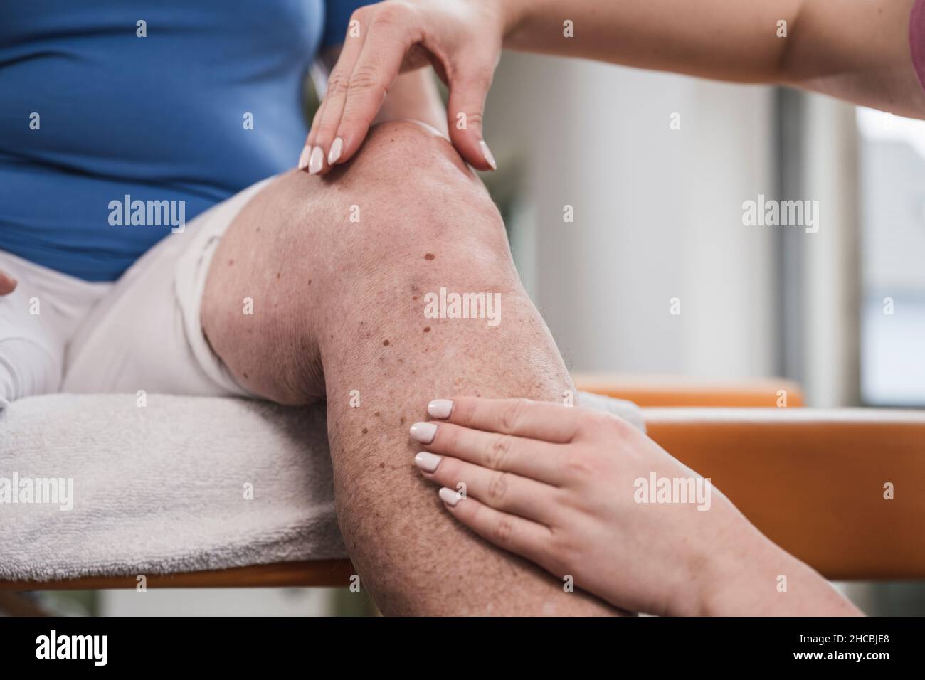Young physical therapist massaging disabled patient's knee at home Stock Photo
