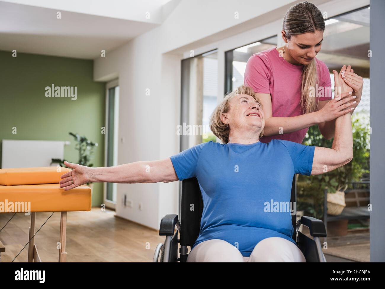 Physiotherapist massaging disabled woman's hand in wheelchair at home Stock Photo