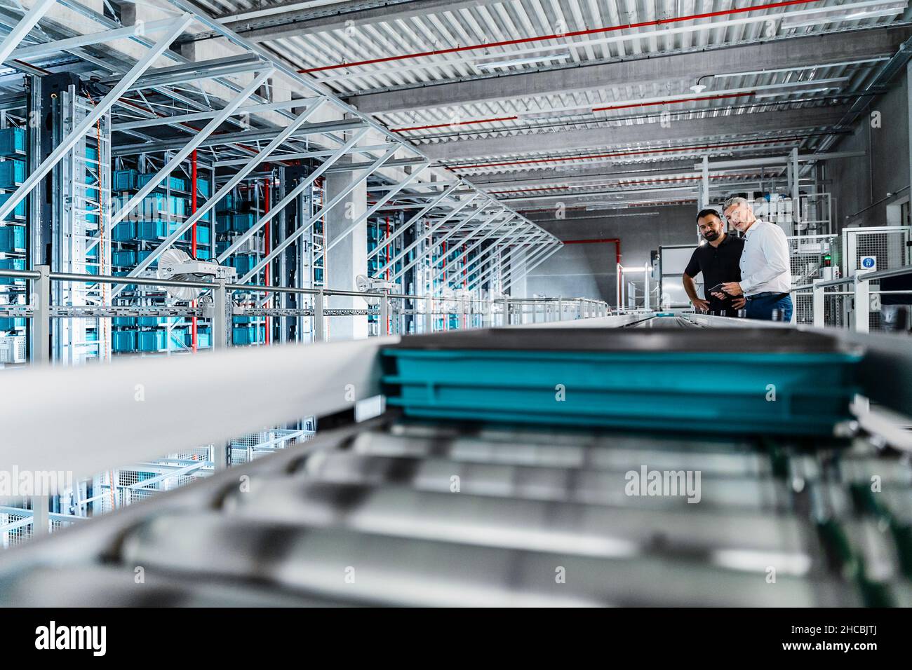 Manager examining equipment on conveyor belt with coworker in warehouse