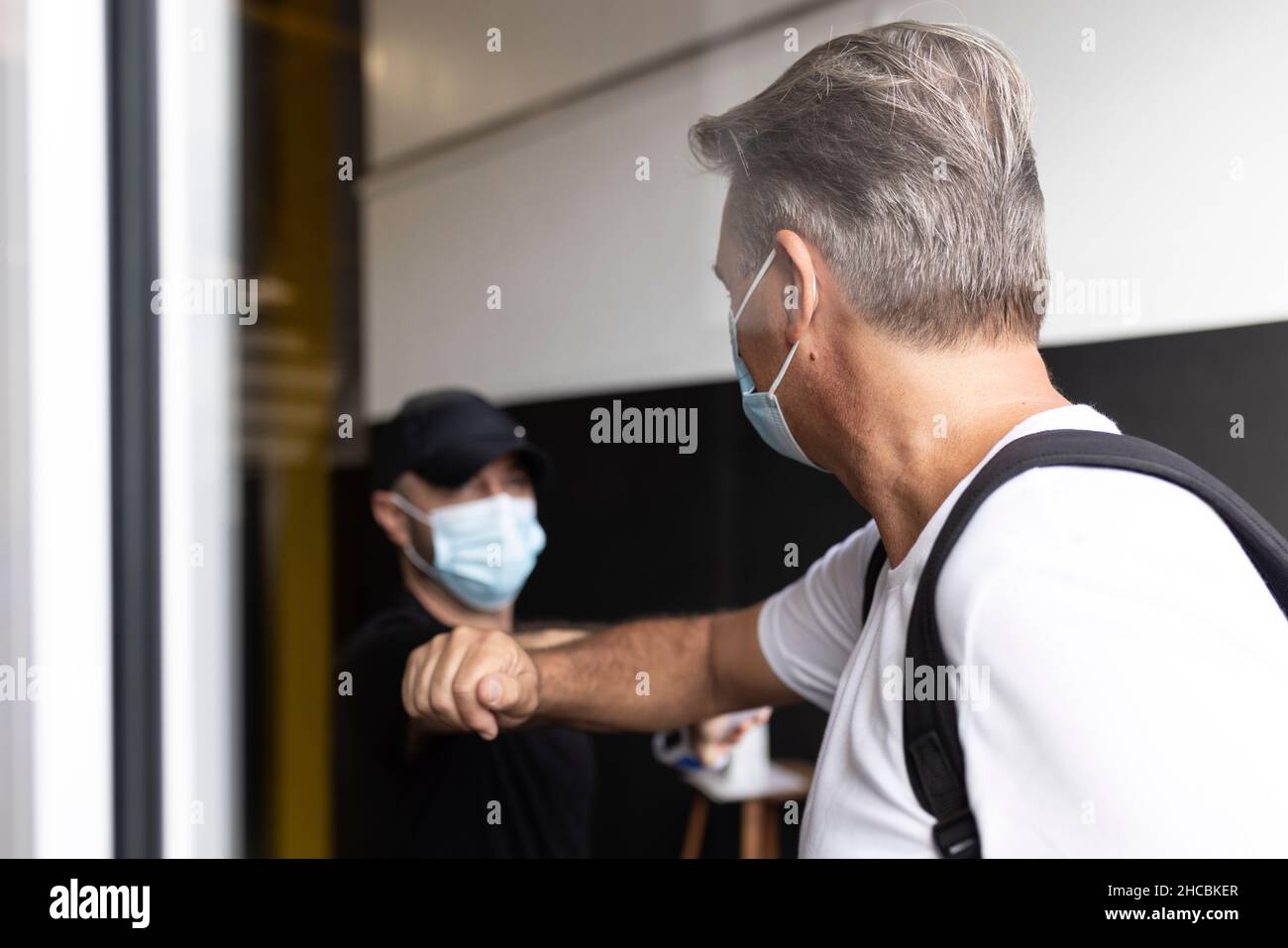 Man taking temperature of woman wearing protective face mask at doorway Stock Photo