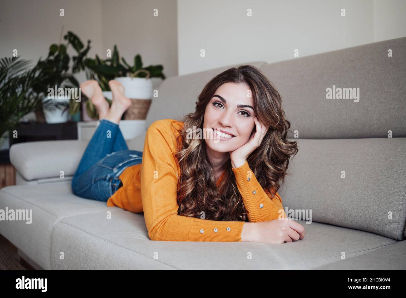Beautiful woman with wavy hair lying on sofa at home Stock Photo