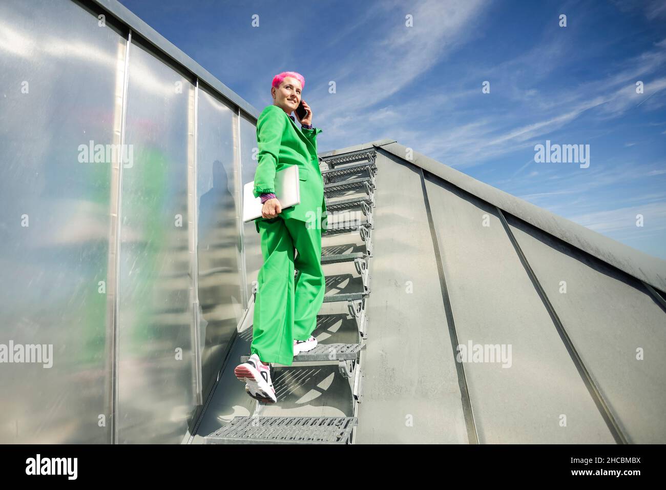 Businesswoman with laptop talking on mobile phone at rooftop steps Stock Photo