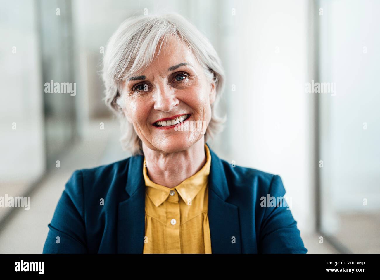 Smiling businesswoman sitting with cross-legged at office corridor Stock Photo
