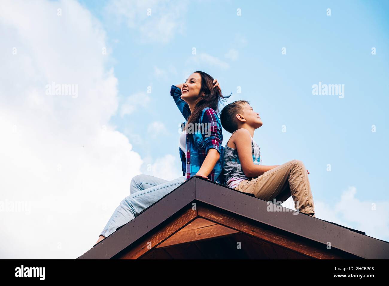 Smiling mother and son sitting back to back on house rooftop Stock Photo