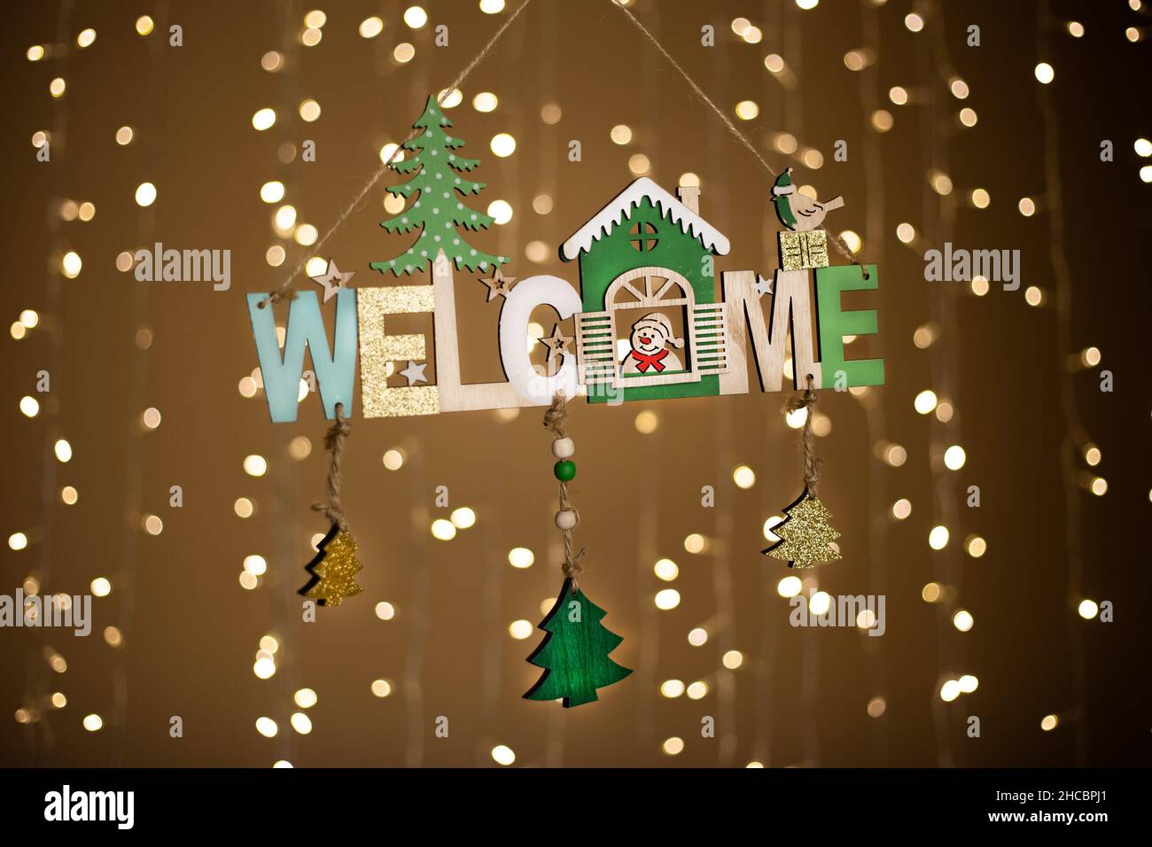 Closeup of a wooden 'WELCOME' Christmas ornament against a blurry background with bokeh lights Stock Photo