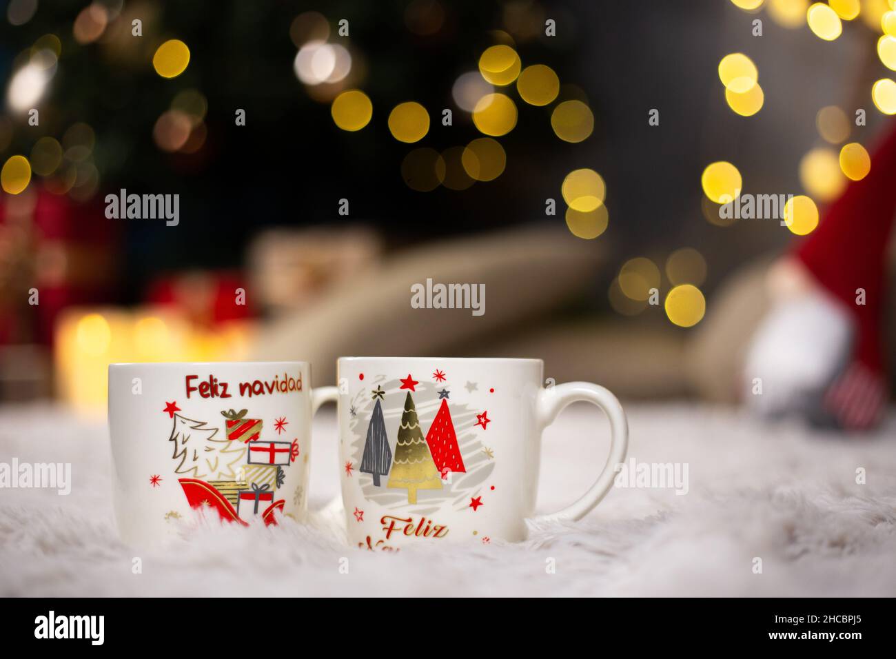 Mugs with Christmas theme prints on a fluffy blanket with a blurry background and bokeh lights Stock Photo