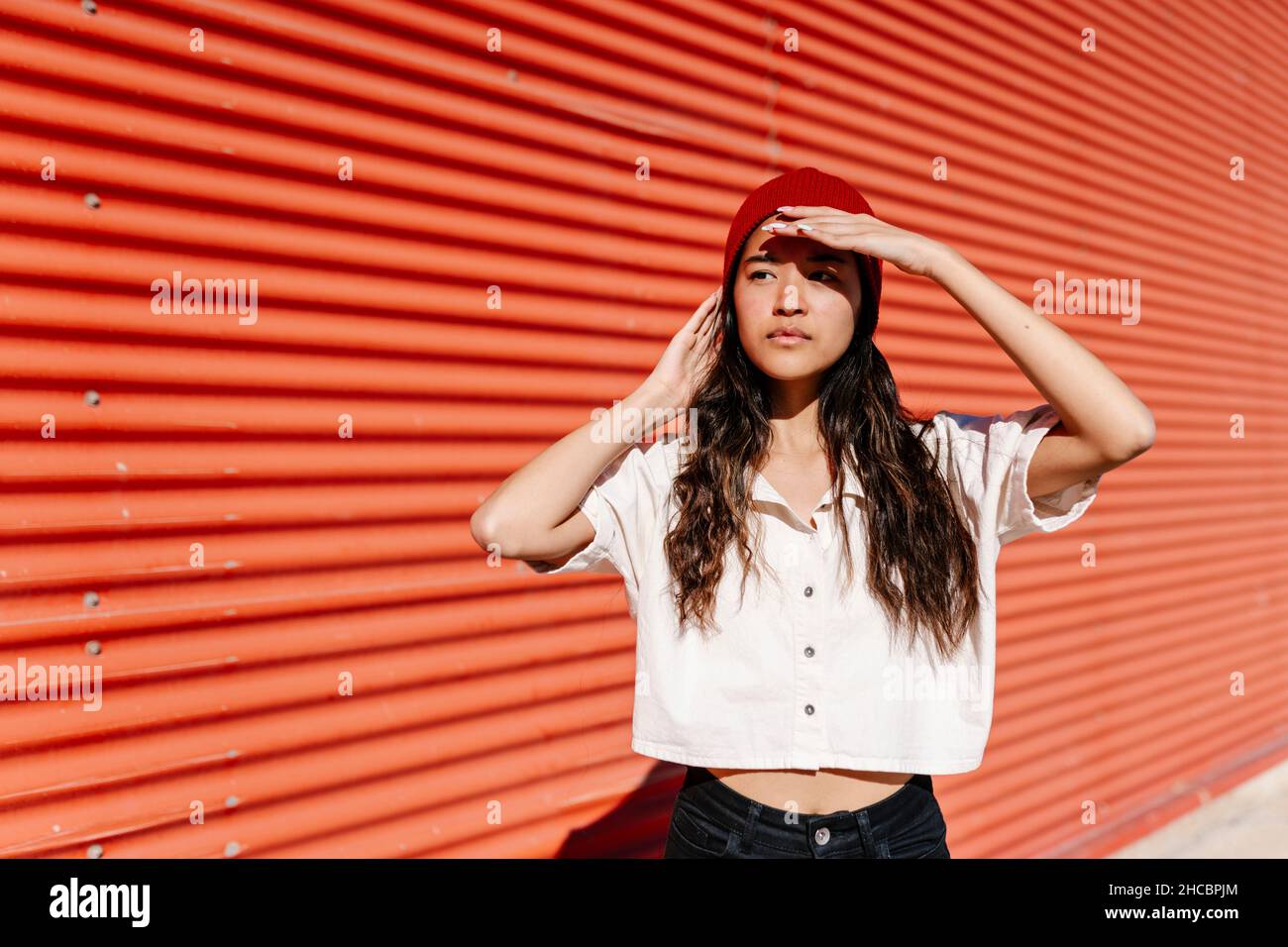 Young woman shielding eyes in front of red corrugated wall Stock Photo