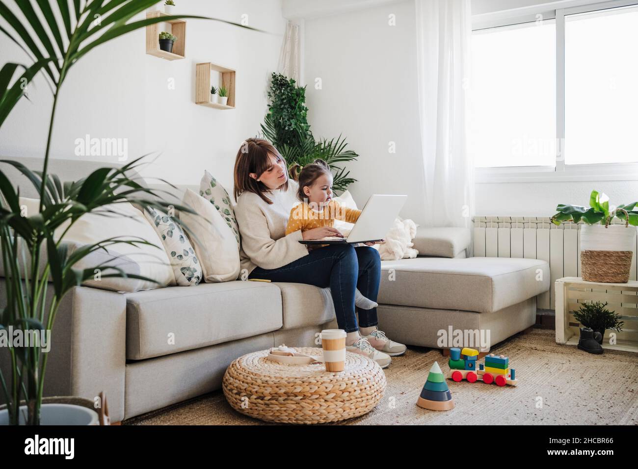 Mother sitting with daughter and using laptop in living room Stock ...