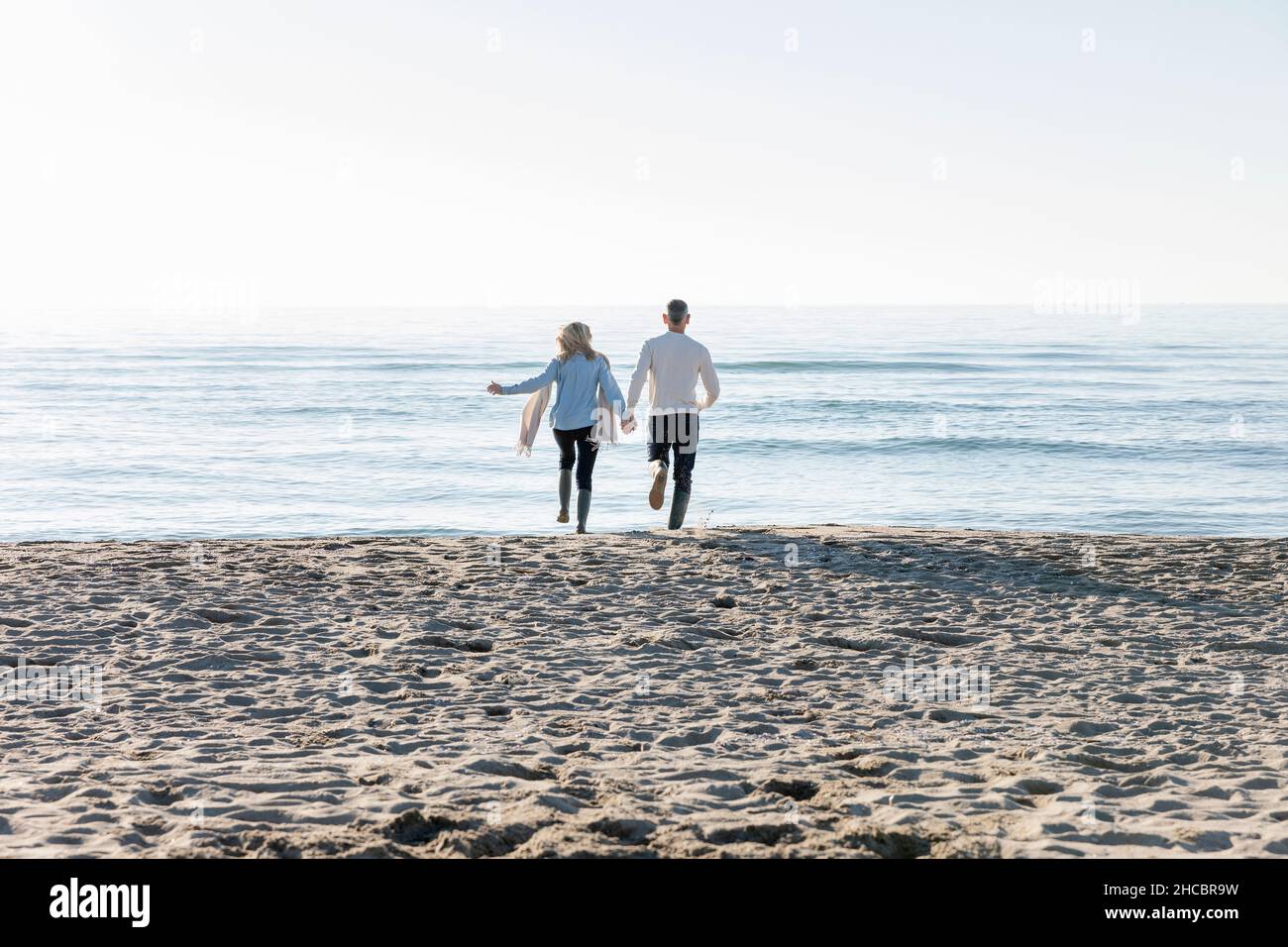 Man and woman running towards sea at beach Stock Photo