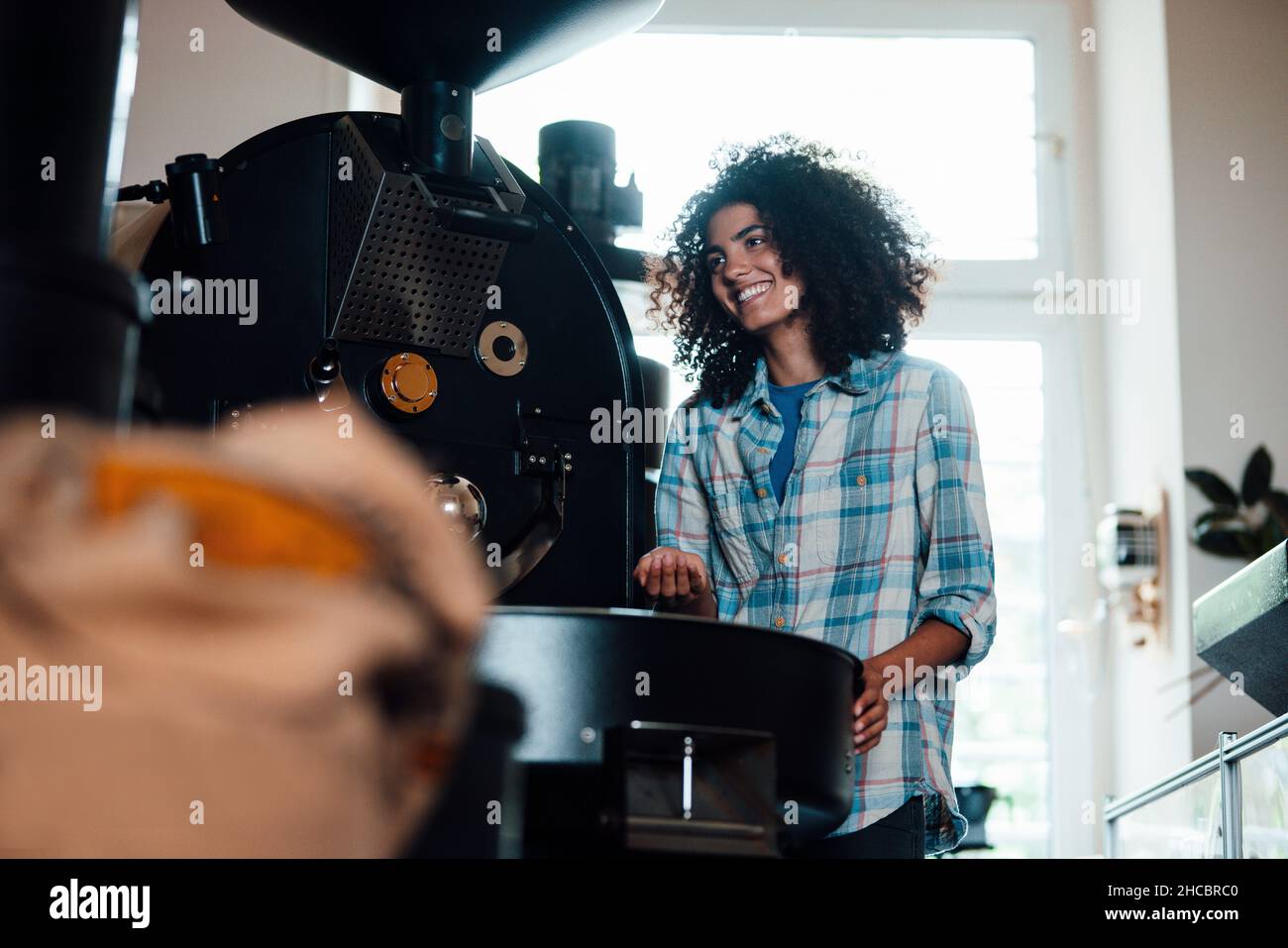 Smiling owner standing near machine in coffee roastery Stock Photo