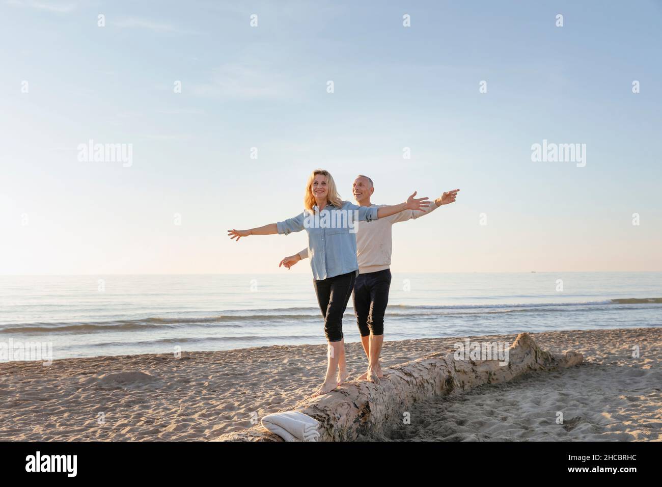 Couple with arms outstretched walking on tree log at beach Stock Photo