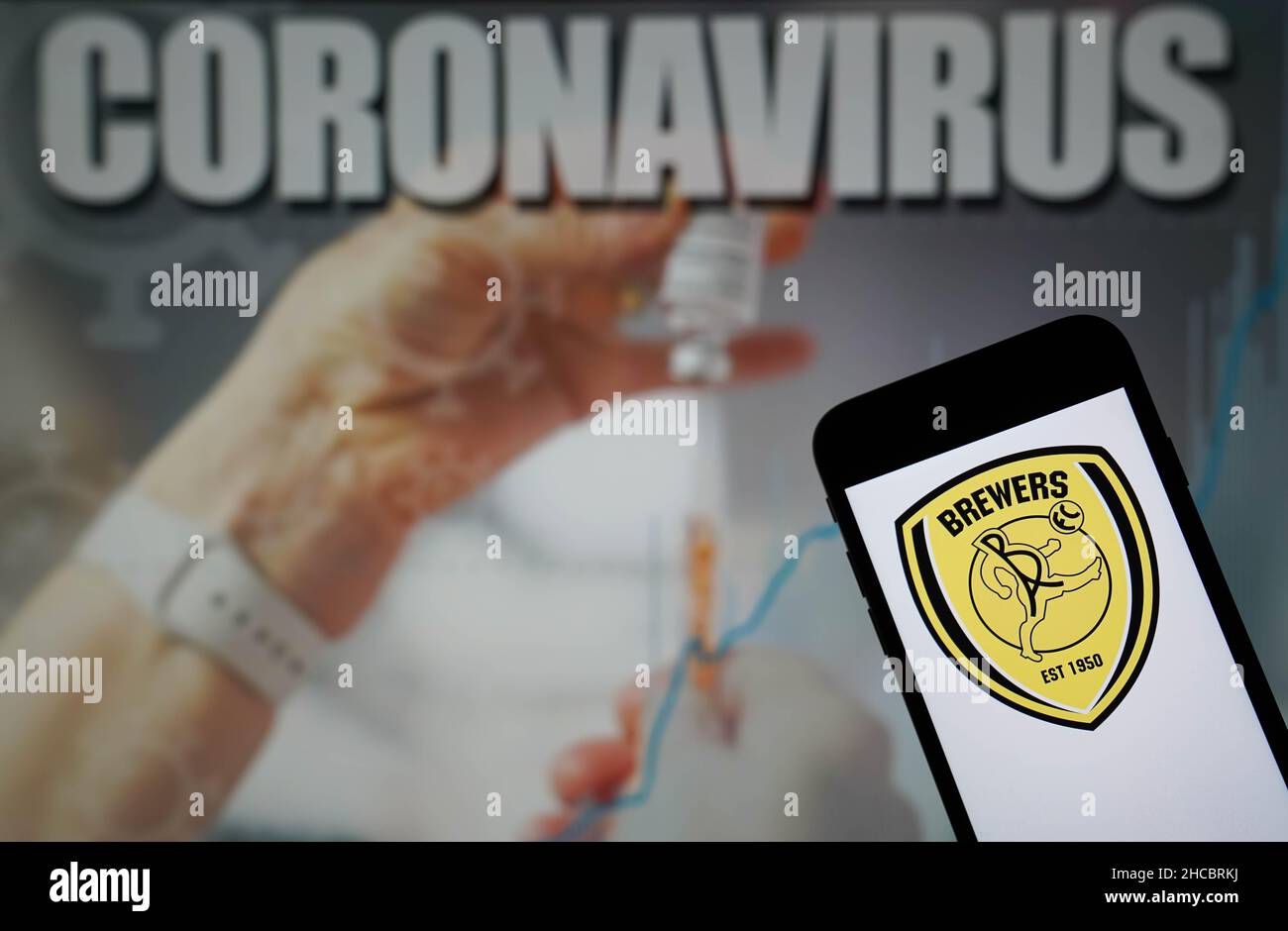 File photo dated 09-01-2021 of The Burton Albion Football Club logo seen displayed on a mobile phone with a Coronavirus illustration on a monitor in the background. Burton's home Sky Bet League One game against Bolton on Wednesday has been postponed due to coronavirus. Issue date: Monday December 27, 2021. Stock Photo