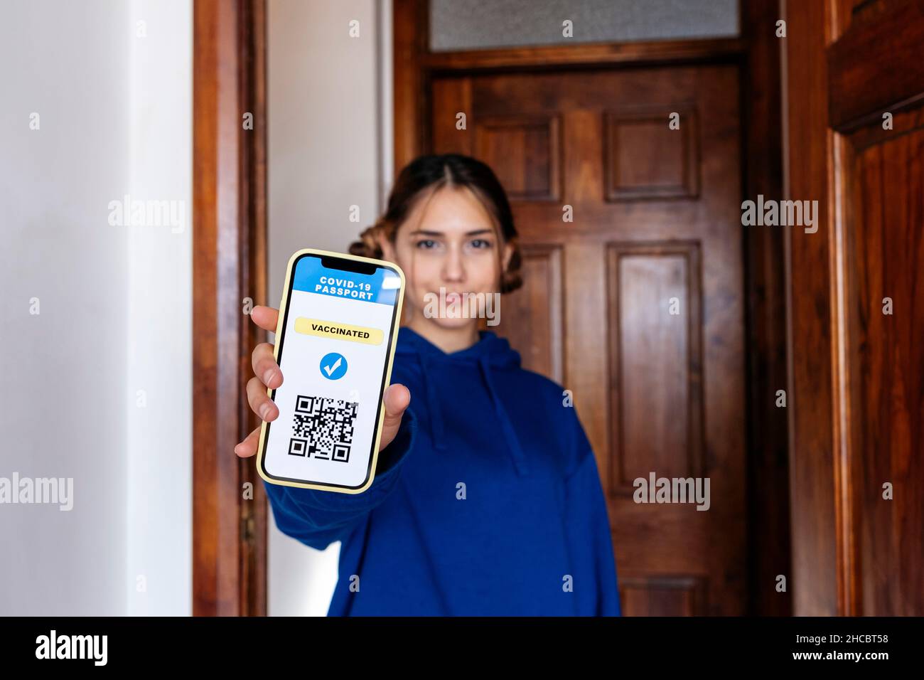 Young woman showing digital vaccine certificate on smart phone at home Stock Photo