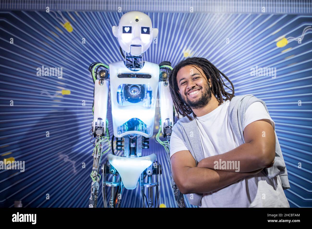 Happy technician with arms crossed leaning near human robot Stock Photo