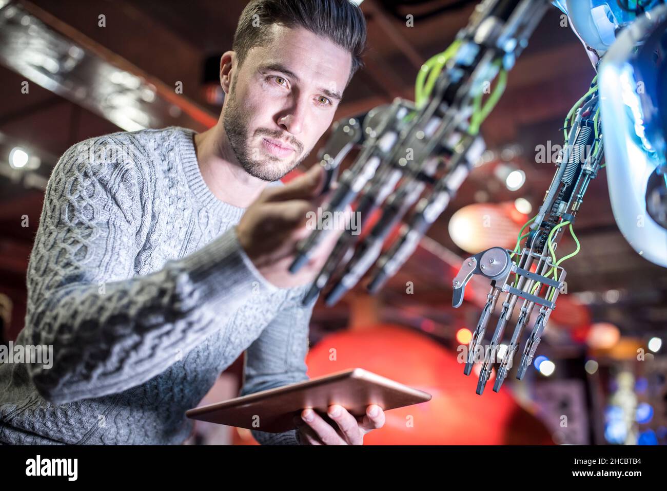 Engineer examining robotic arm holding tablet PC at workshop Stock Photo