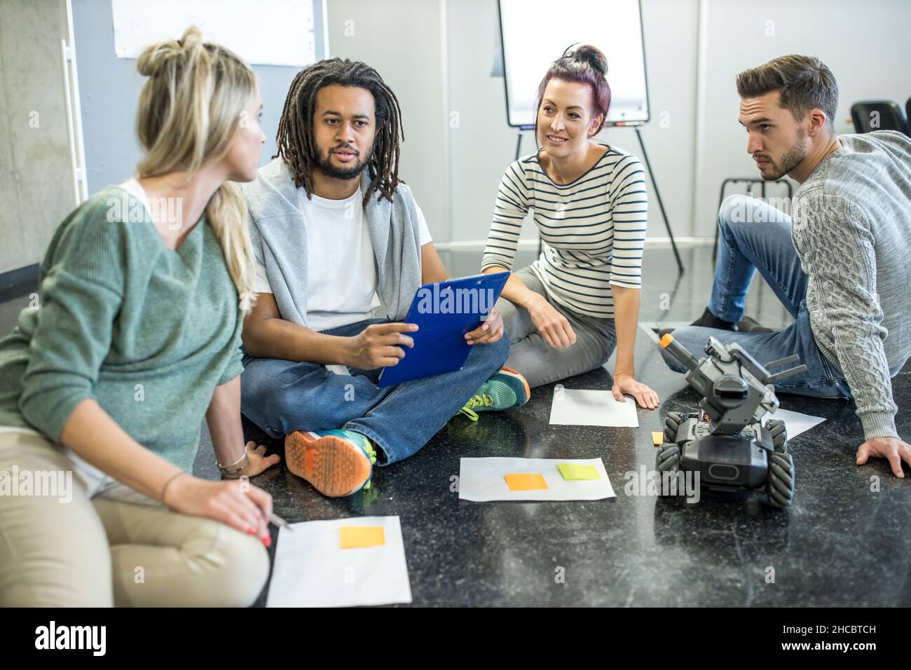 Engineers and technicians discussing with each other sitting at robotic ...