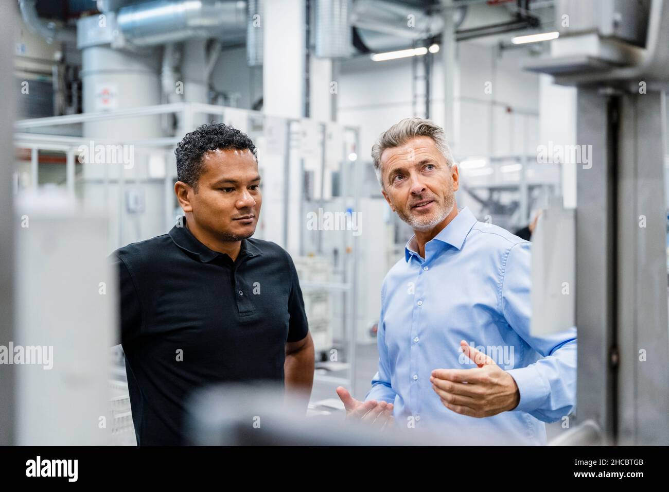 Businessman explaining engineer and looking at machine in industry Stock Photo