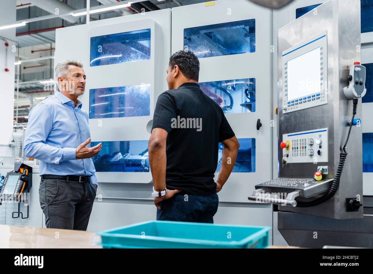 Businessman explaining engineer by machine in industry Stock Photo