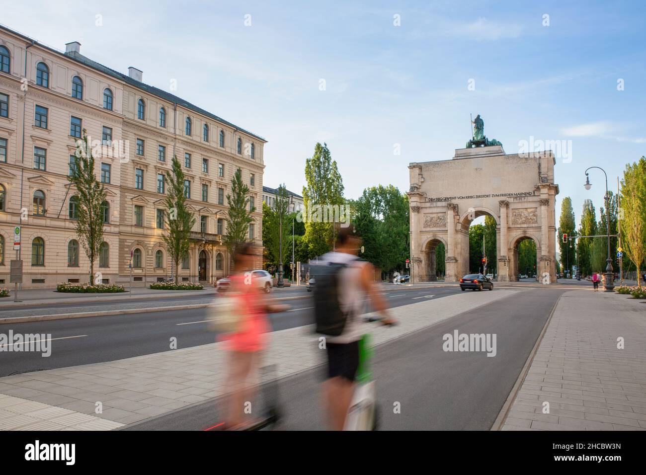 Germany, Bavaria, Munich, Two people riding electric push scooters towards Siegestor gate Stock Photo