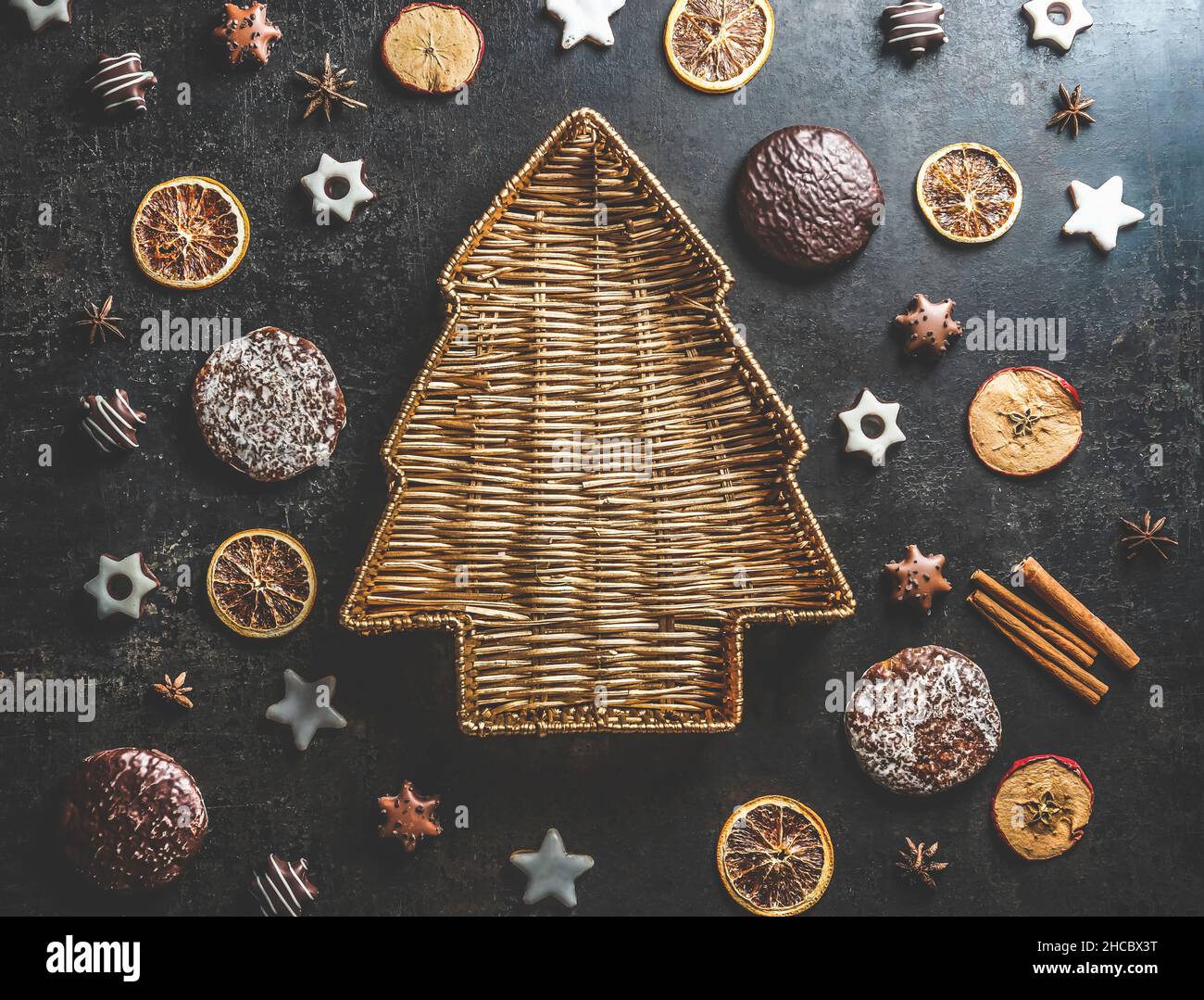 Christmas tree shaped wooden tray on dark concrete table with gingerbread, cookies, dried orange slices and cinnamon sticks. Delicious seasonal winter Stock Photo