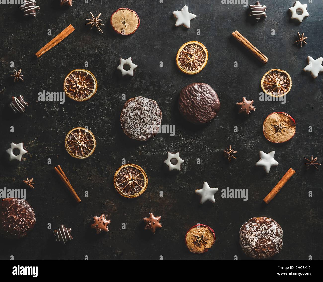 Christmas pattern made with dried orange, cinnamon sticks, gingerbread and Christmas cookies on dark kitchen table background. Top view. Stock Photo