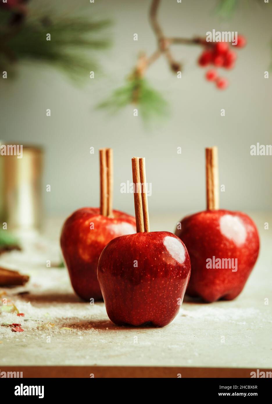 Red apples with cinnamon sticks on kitchen table with sugar at wall background with fir green. Sugar glazed apples. Delicious Christmas sweets. Front Stock Photo