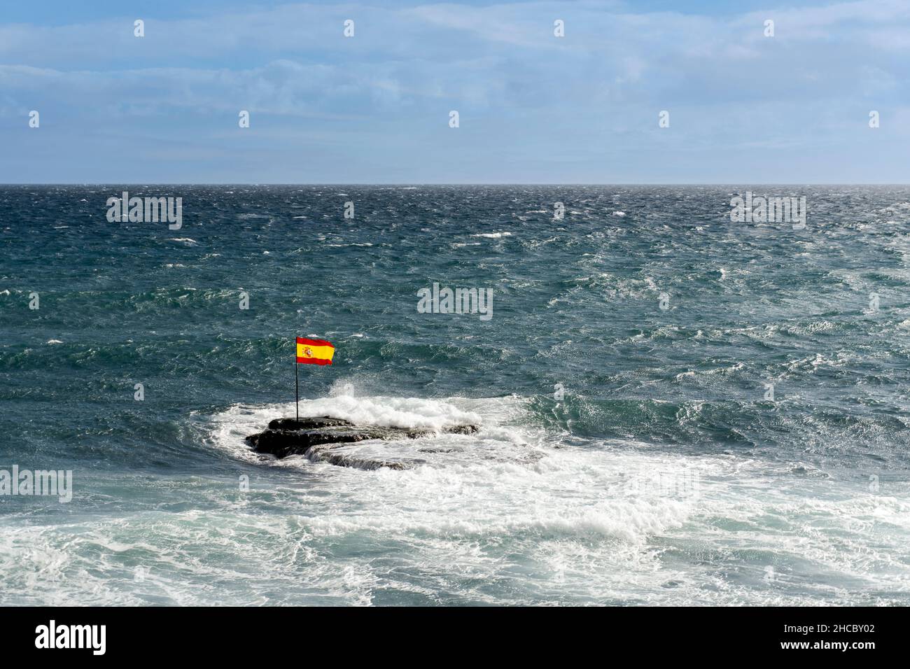 A Spanish flag on rocks in the Atlantic Ocean during windy weather in
