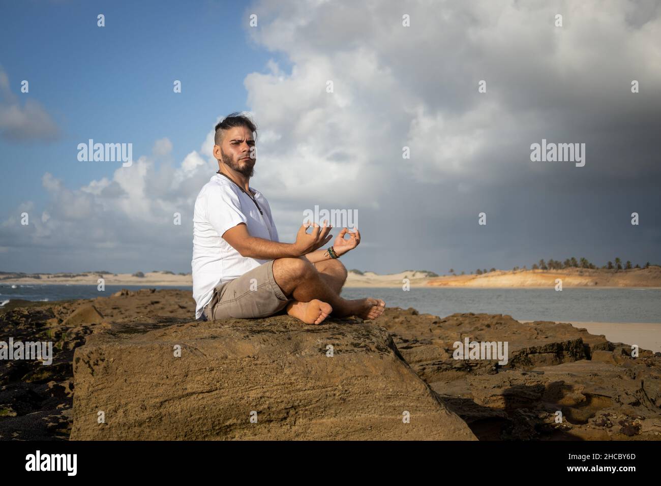 White man between 25 and 30 years old at the edge of the sea doing yoga. Meditation in nature. Stock Photo