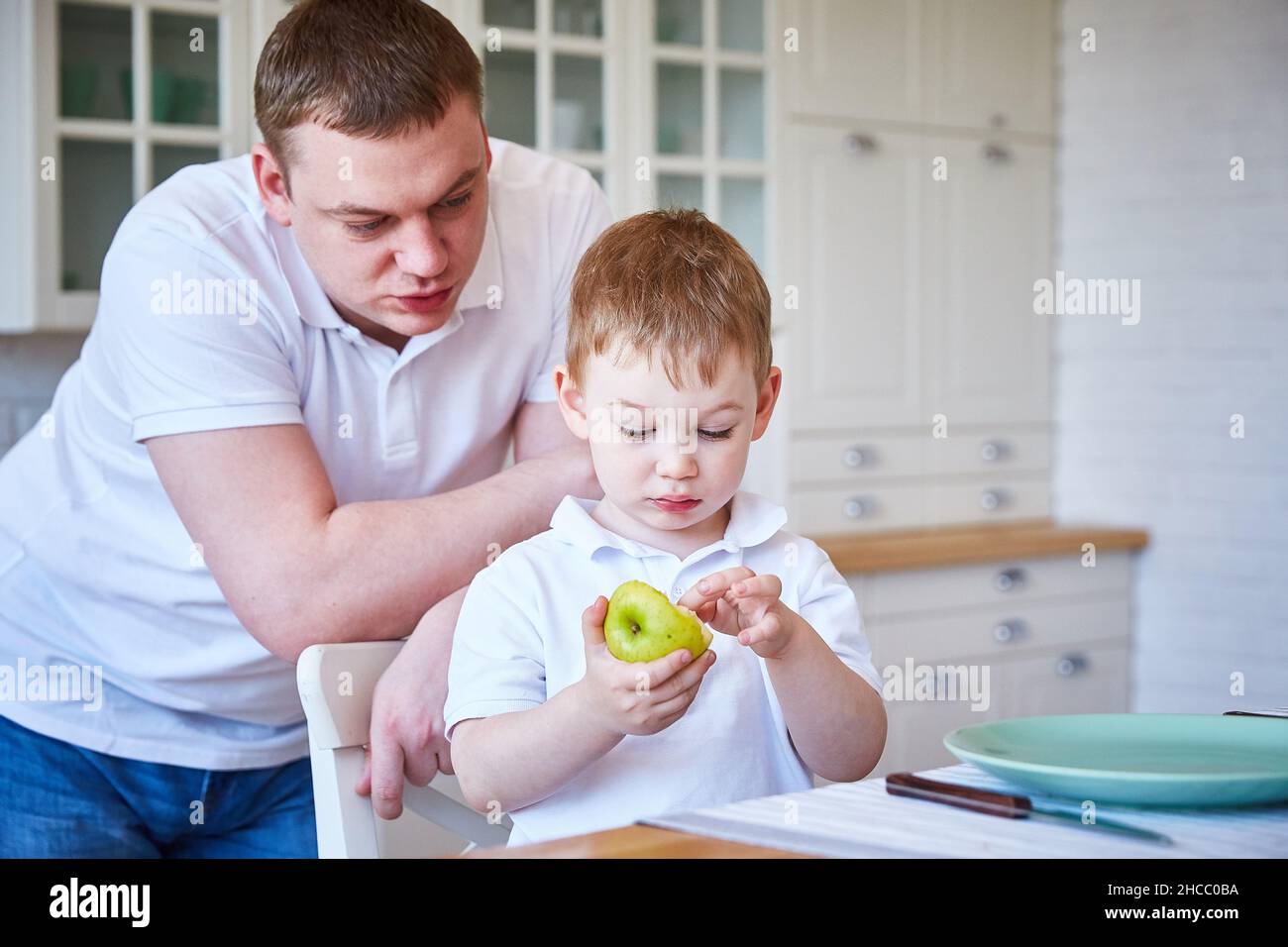 boy with his father in the kitchen. The child eats an apple. Copy space Stock Photo