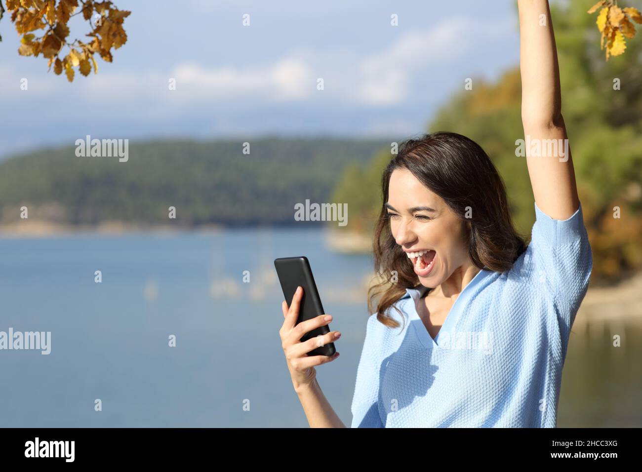 Excited woman checking smart phone celebrating good news outdoors Stock Photo