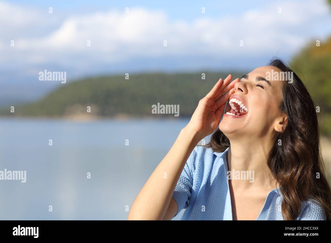 Happy woman screaming to the air with hand on mouth in a mountain lake Stock Photo