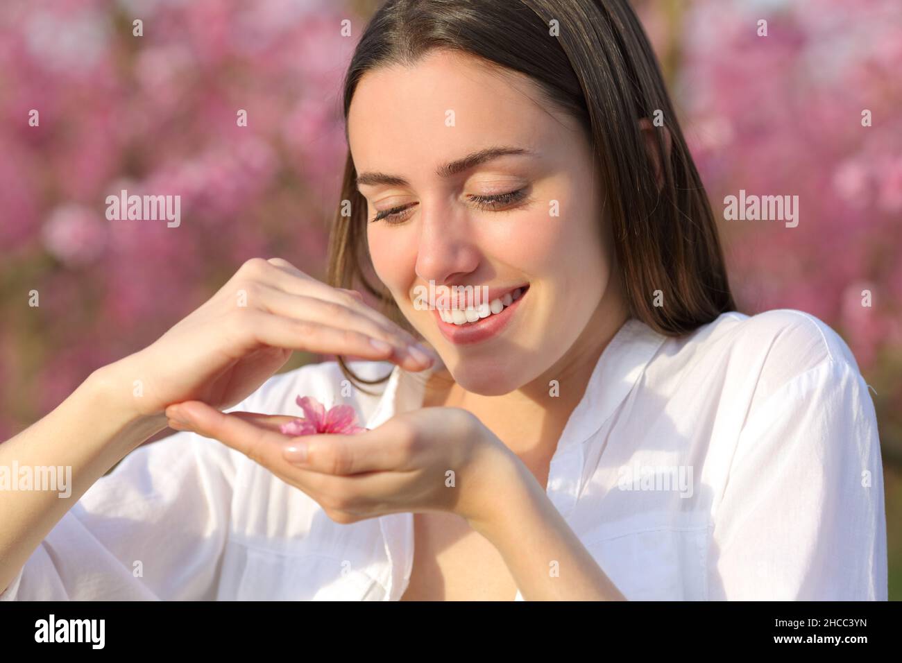 Happy woman holding and protecting flower in a pink field Stock Photo