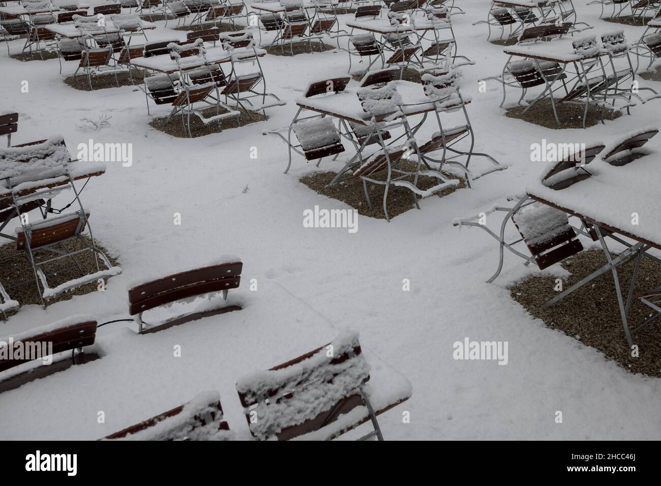 Tables and chairs suites of closed Bavarian beer garden in public park in Regensburg in winter with fresh snow Stock Photo