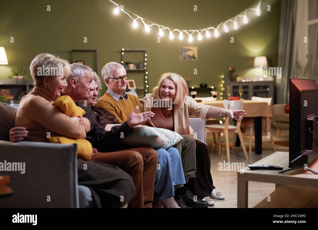 Two aged men and three women sitting together on couch in front of TV, watching interesting movie and discussing it Stock Photo
