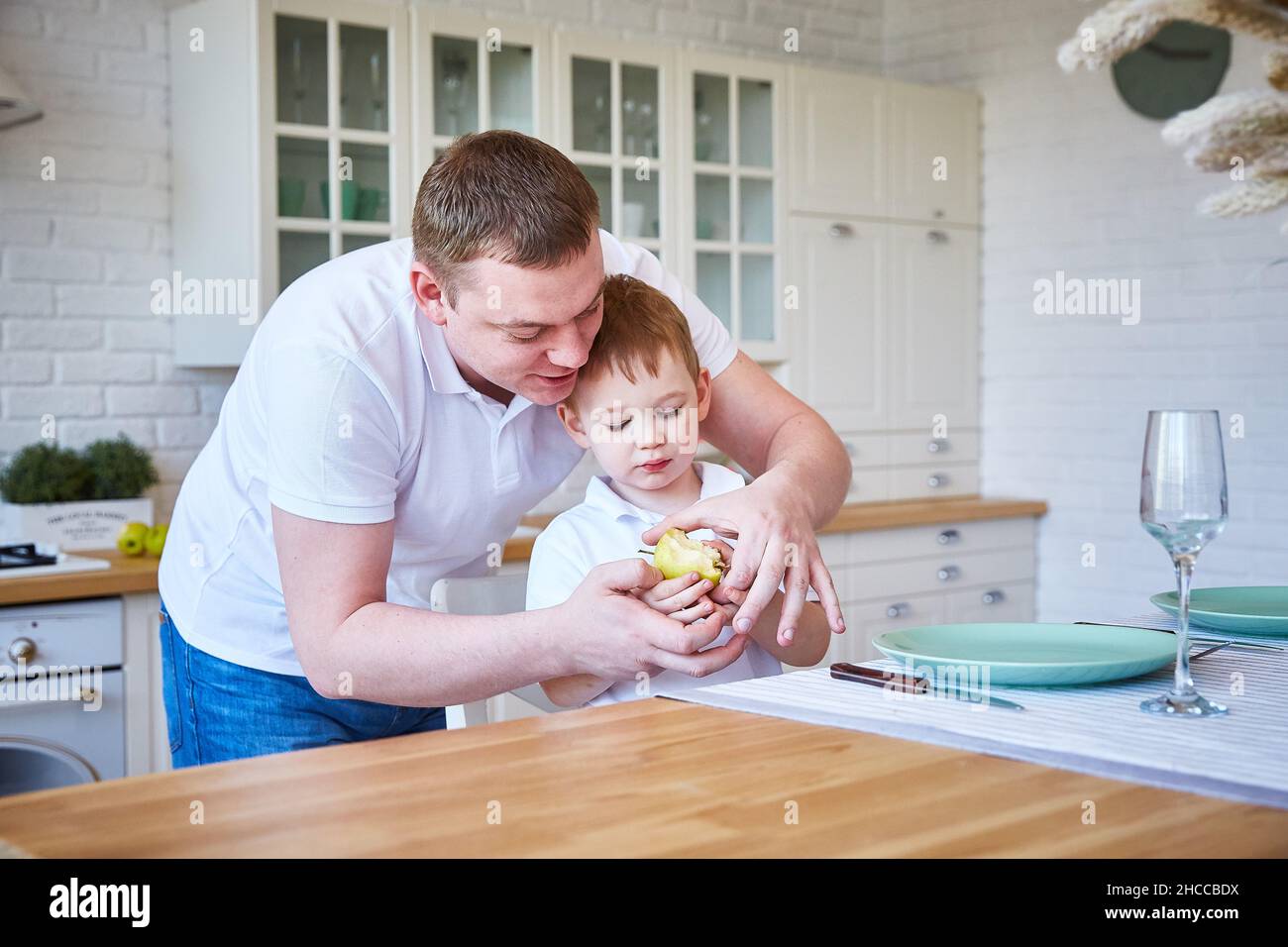 boy with his father in the kitchen. The child eats an apple. The concept of family and fatherhood. Copy space Stock Photo