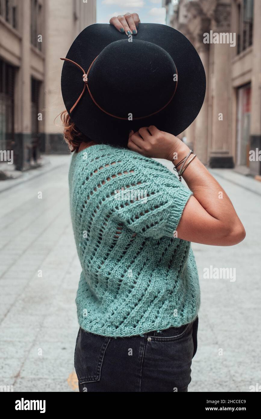 Image of a woman hiding her face with a black hat in the middle of a lonely street Stock Photo