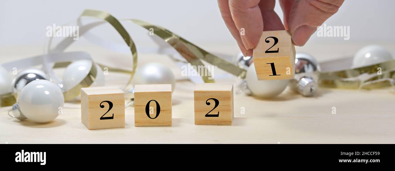 Hand is turning wooden cubes from 2021 to 2022 for the new year in panoramic format, seasonal decoration against a gray background, copy space, select Stock Photo