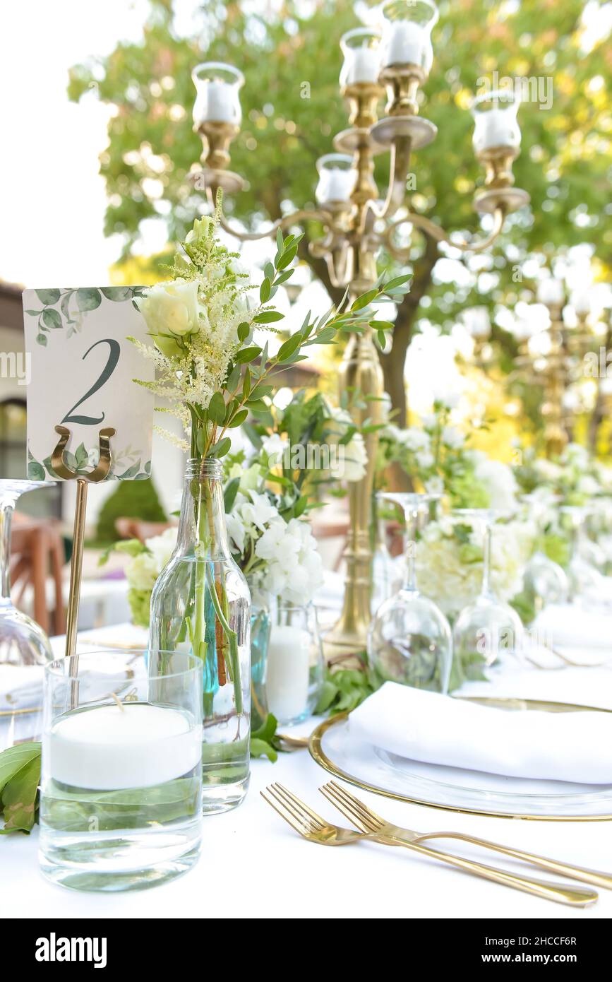 A vertical shot of table settings decorated with flowers and candles on a white tablecloth and a sign showing '2' ready for an event Stock Photo