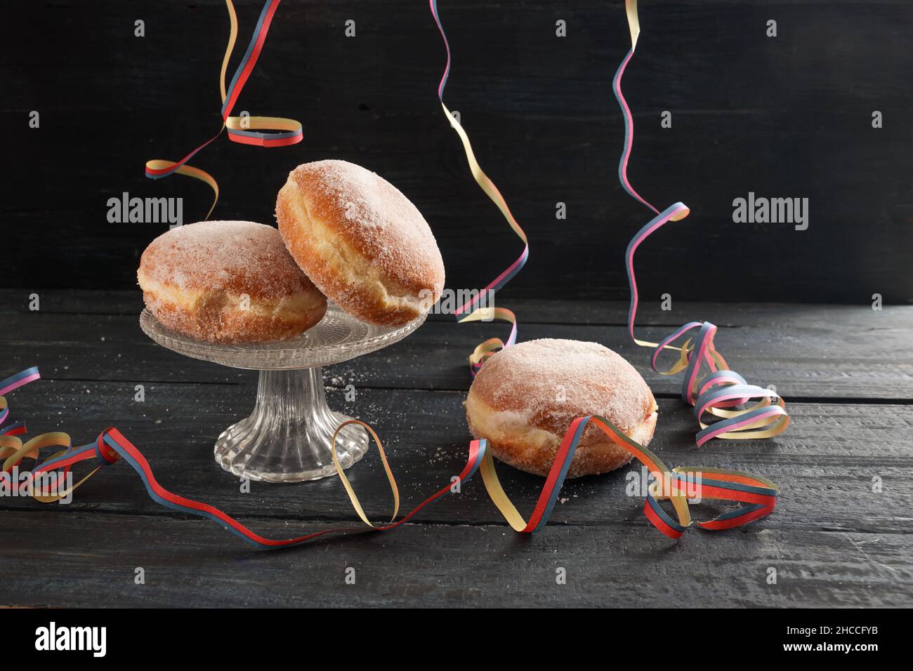 Berliner doughnuts or Krapfen with colorful party streamers on a dark rustic wooden table, traditional pastry for New Year or carnival, copy space, se Stock Photo