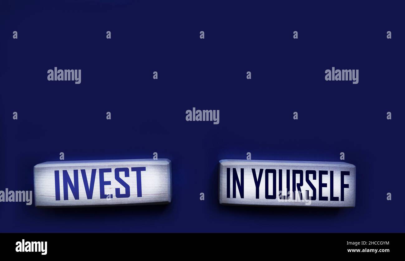 Invest in yourself. Motivational words in wooden alphabet letters isolated on blue background Stock Photo