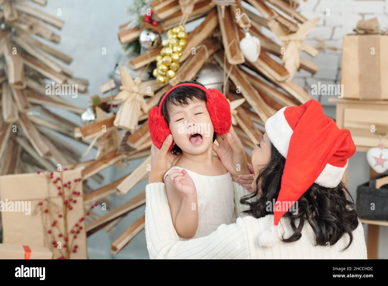 Mother trying to put red faux fur ear muffs on head of crying and