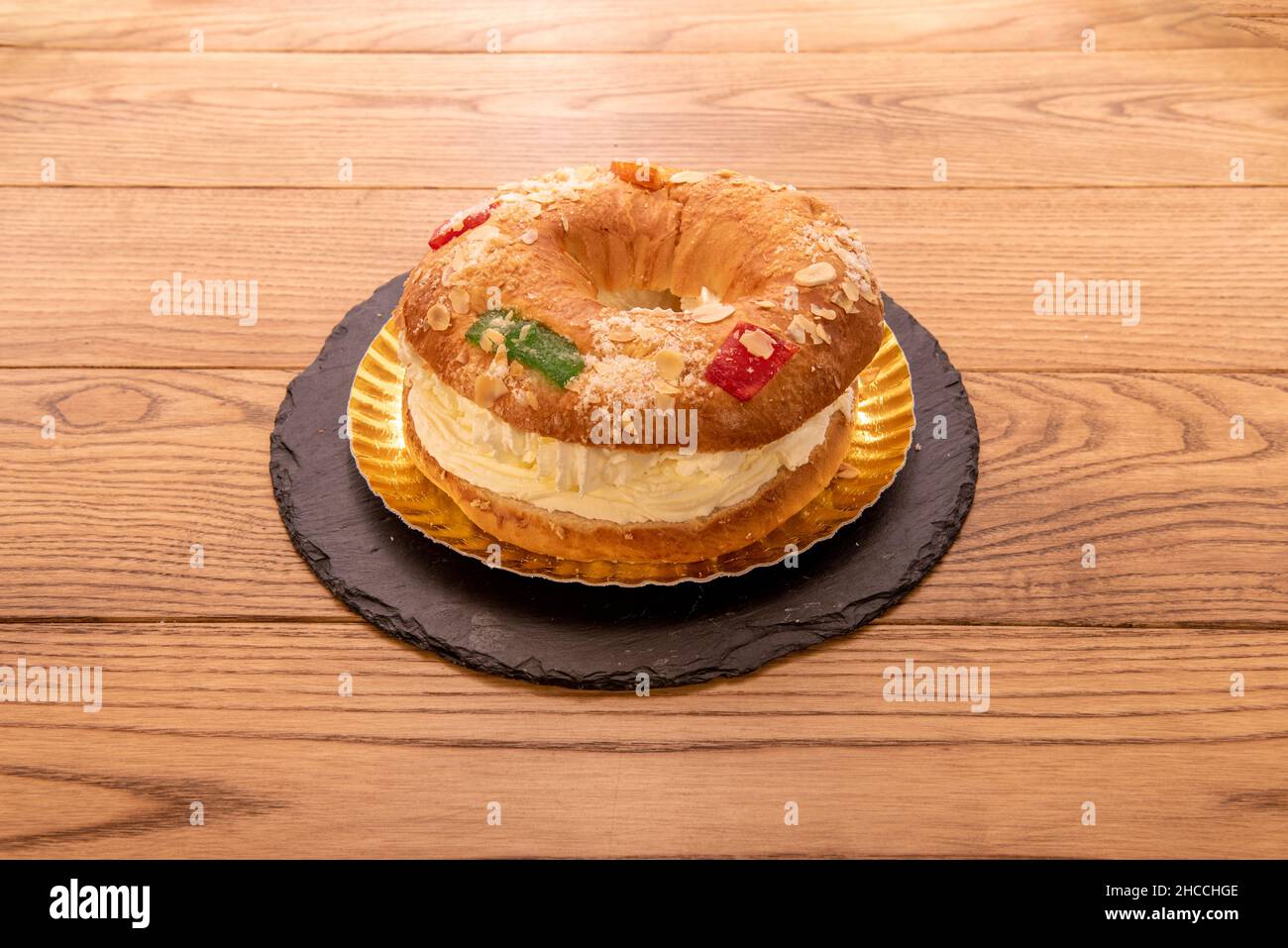 Roscón filled with cream with almonds, candied fruits, icing sugar and a golden tray and plate of black pizza Stock Photo