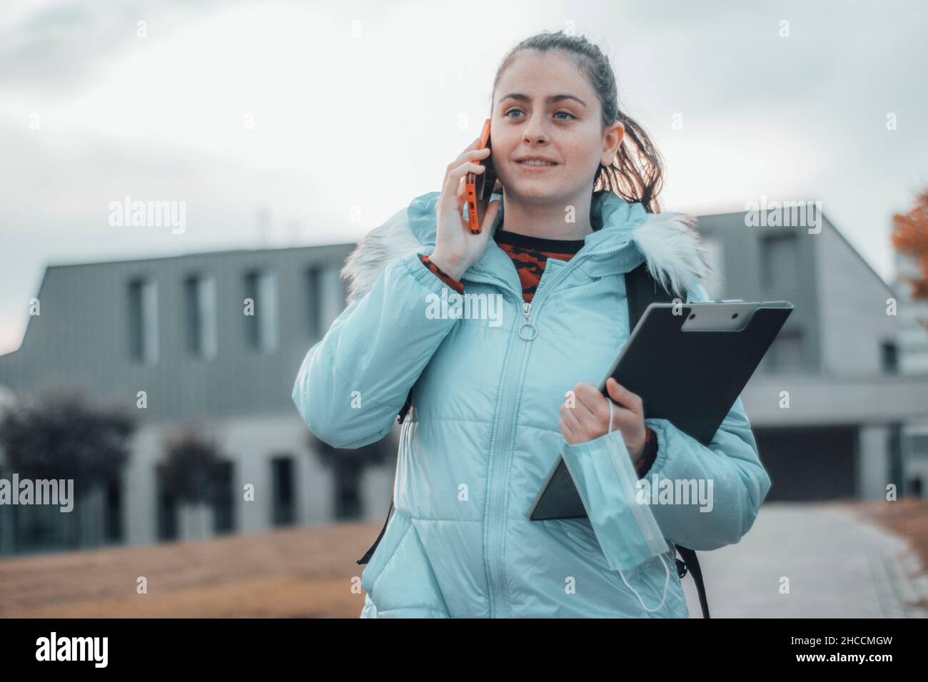 Young girl medical student outdoors resting at recess while calling on the mobile phone with joy together with her notes and folder Stock Photo