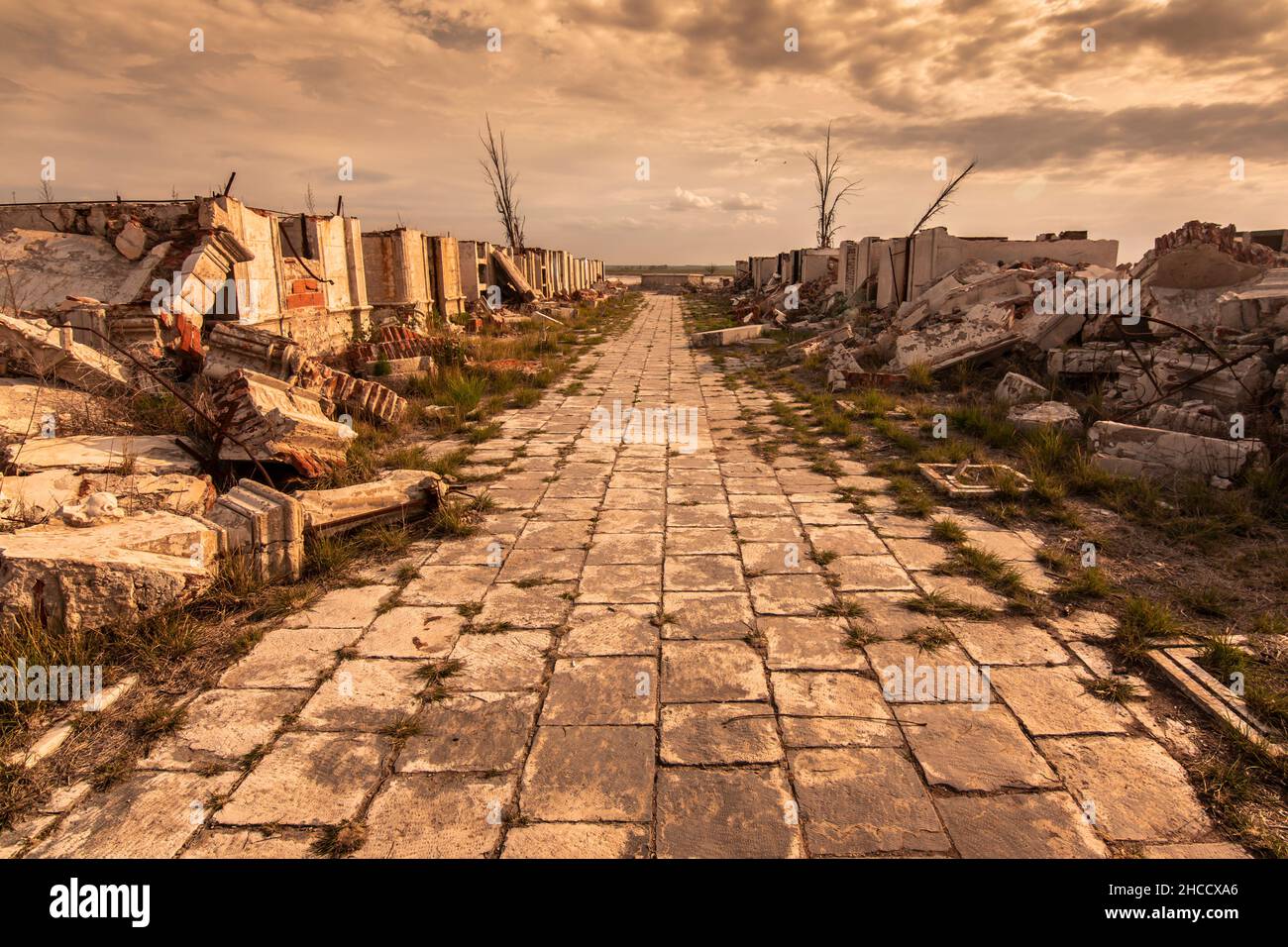 Path between demolished buildings with expressive sky and dry trees. Abandoned cemetery in Carhué, Buenos Aires, Argentina. Stock Photo
