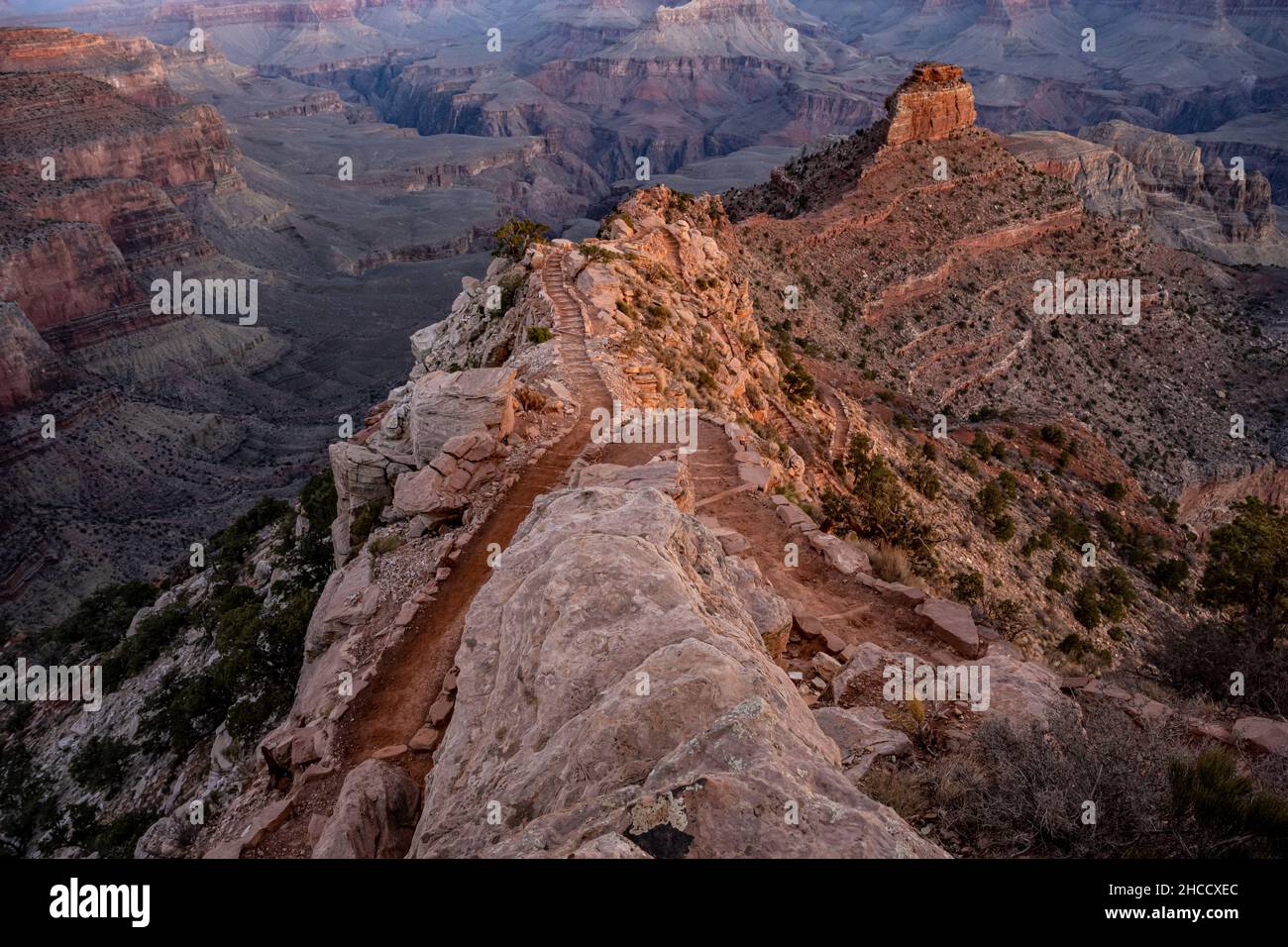 Rock Overlooking the South Kaibab Trail as it Winds down into the Grand Canyon in morning light Stock Photo