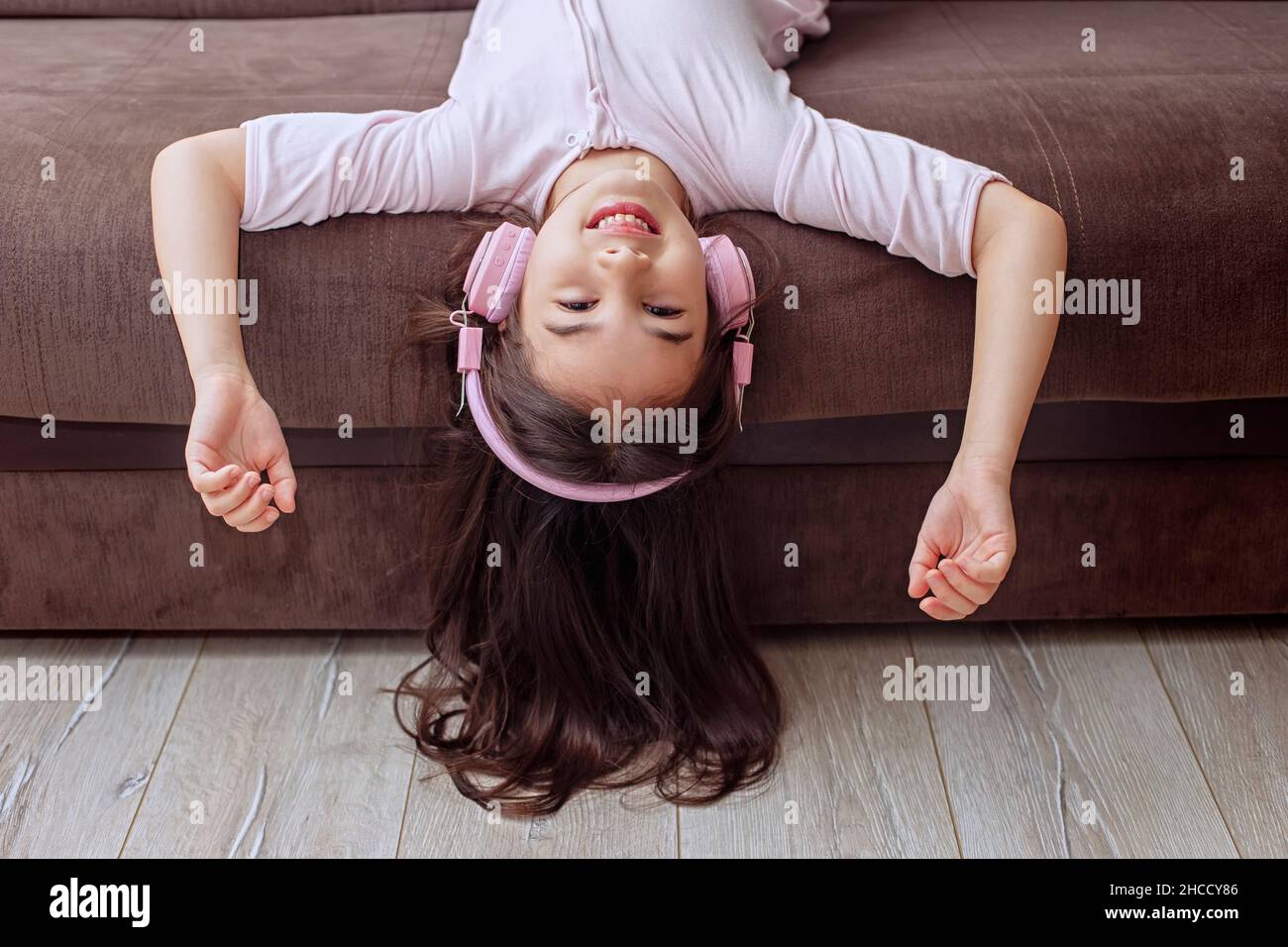 A funny little girl in pink home clothes and pink headphones, lies on the couch Stock Photo