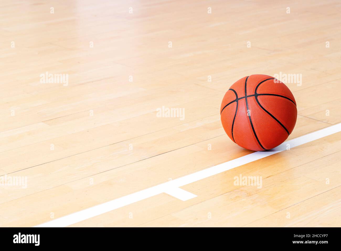 Basketball on hardwood court floor with natural lighting. Workout